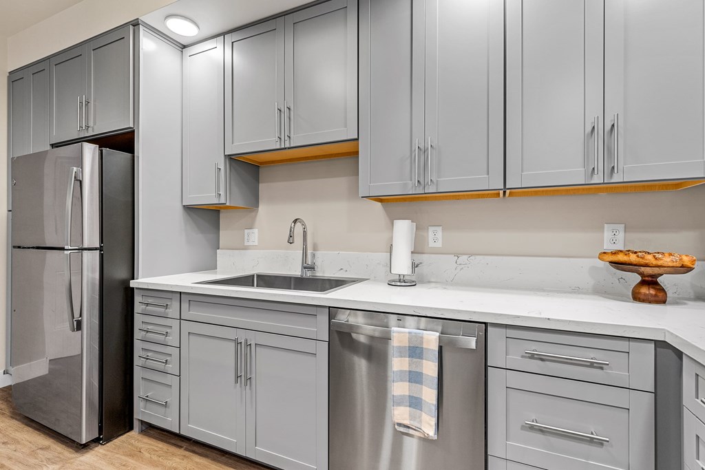 A kitchen with grey cabinets and a stainless steel refrigerator.