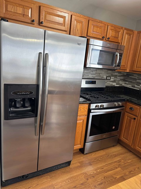 A stainless steel refrigerator with a freezer drawer and a water dispenser is in a kitchen with wooden cabinets.