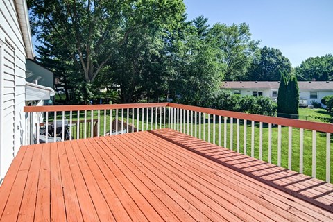 A wooden deck with a white railing and trees in the background.