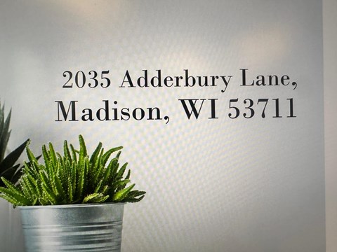 A plant in a metal pot is in front of a grey background with the address 2035 Adderbury Lane, Madison, WI 53711 displayed.