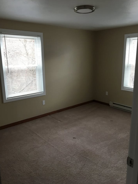 A room with a carpeted floor and two windows.