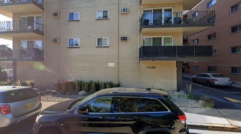 A black car is parked in front of a building with the number 7420 on it.