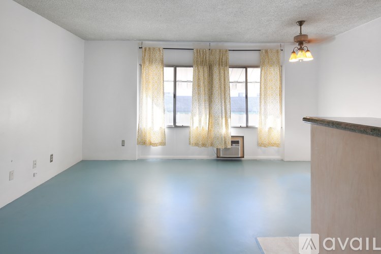 A room with a window and curtains, a fan, and a chair.