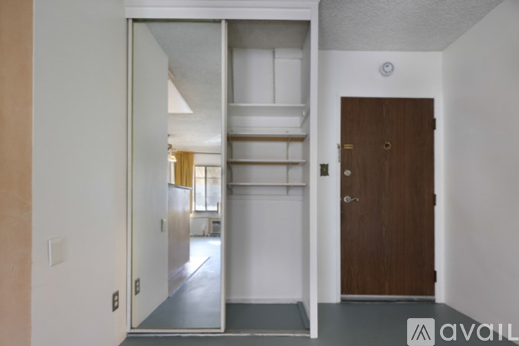 A hallway with white walls and a blue floor leading to a door with a gold handle.