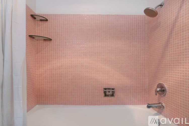 A pink tiled shower area with a white tub and a shower head.