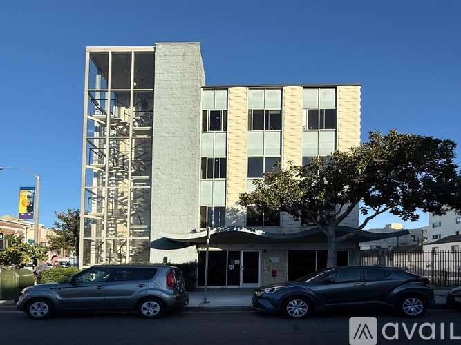 A modern building with a tree in front of it and two cars parked in front of the building.