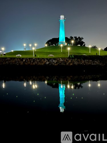 A lighthouse is lit up at night with its reflection visible in the water.
