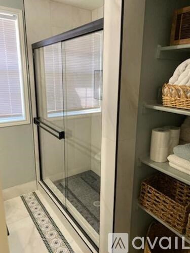A bathroom with a glass shower door and shelves with towels and baskets.