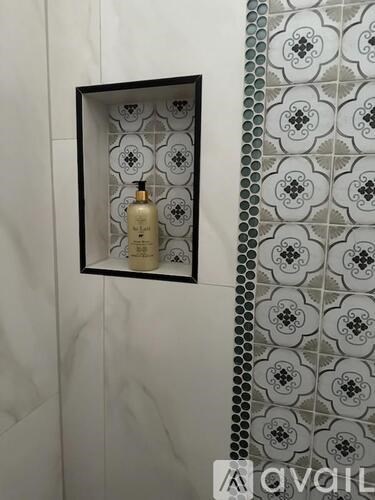 A bottle of perfume is displayed in a black frame on a tiled wall.