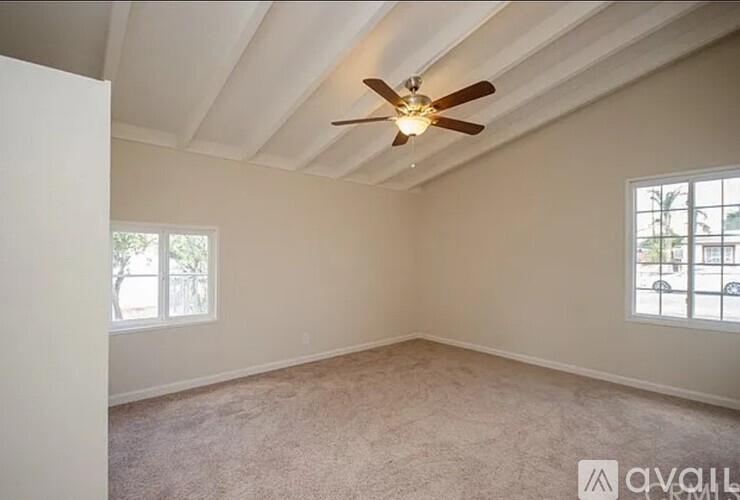 A room with a ceiling fan and two windows.