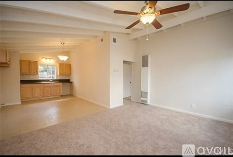 A spacious living room with a ceiling fan and carpeted floor.