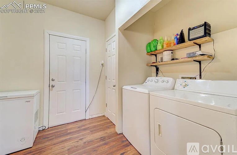 A laundry room with a washer and dryer, a door, and a shelf with various items.