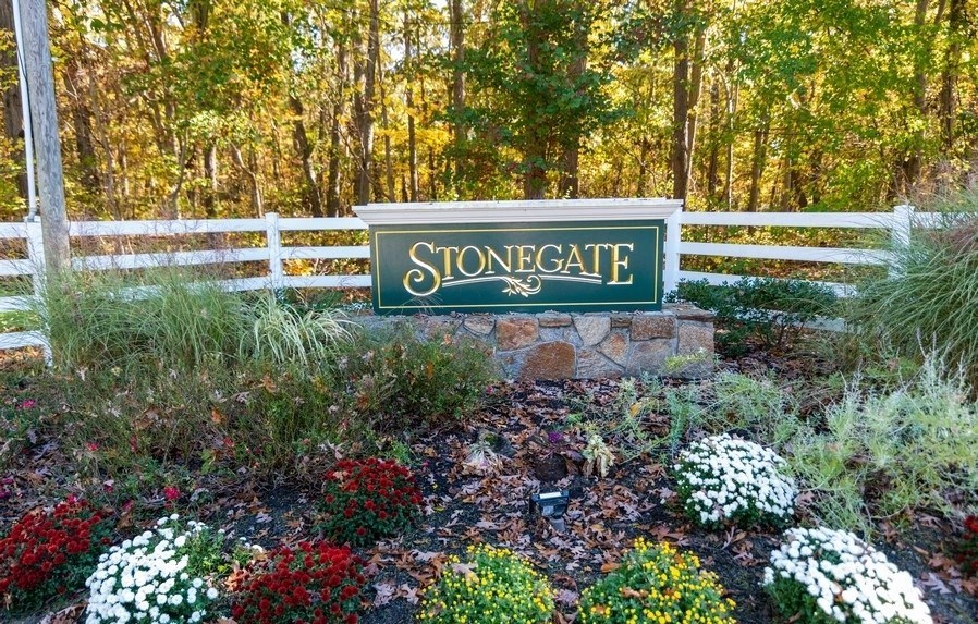 a sign for stonegate in front of a fence and trees