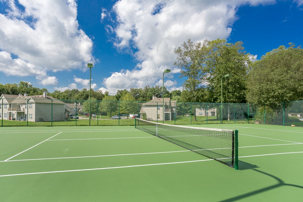 two tennis courts with houses and trees in the background on a sunny day