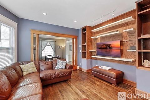 A brown leather couch sits in a living room with a wooden wall and a painting hanging above it.