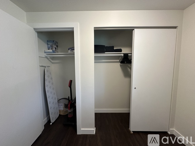 A small, white closet with a towel hanging on a rod and a broom on the floor.