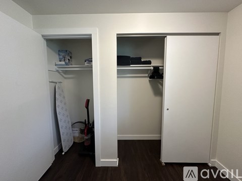 A small, white closet with a towel hanging on a rod and a broom on the floor.