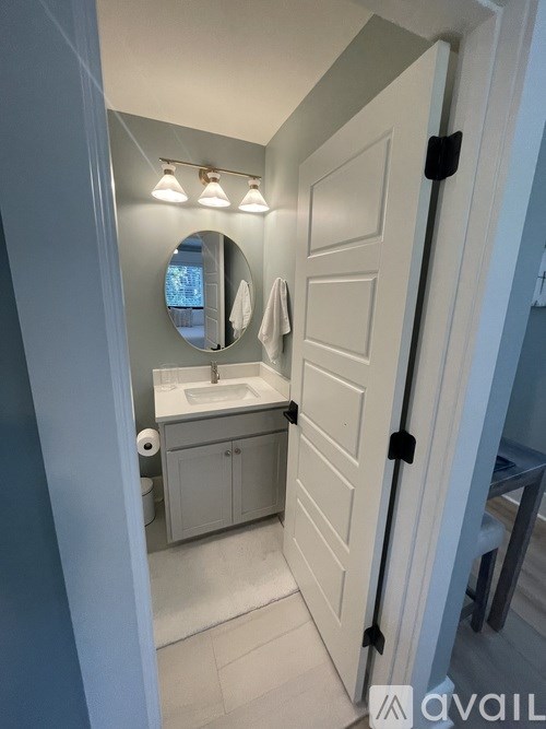 A bathroom with a white door and a round mirror above the sink.