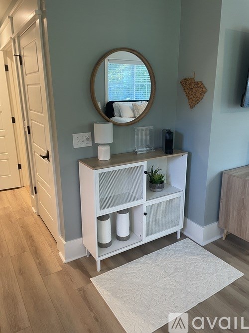 A white cabinet with a round mirror above it and a plant on the shelf.