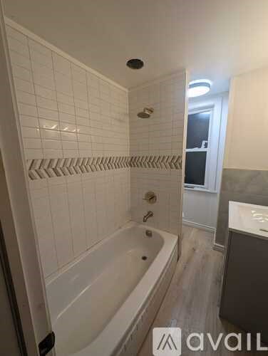 A bathroom with a white tub and a white tiled wall.