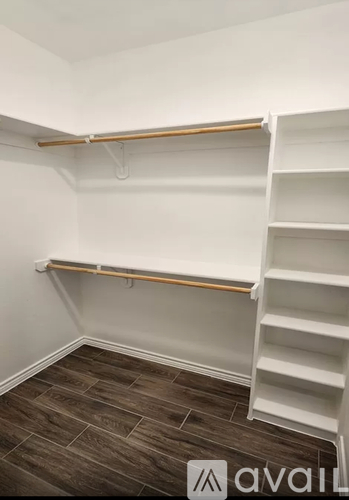 A white shelving unit with wooden supports is in a room with a wooden floor.