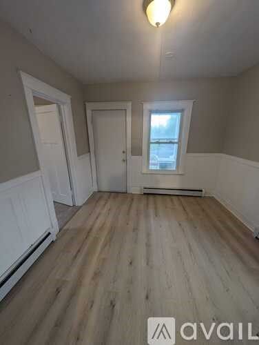 A room with wooden floors and white walls, with a window and two doors.