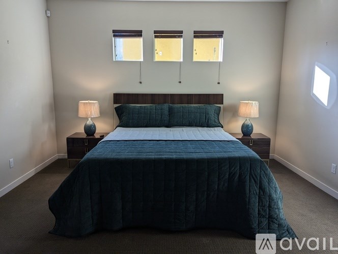 A bedroom with a bed, two lamps, and two windows.