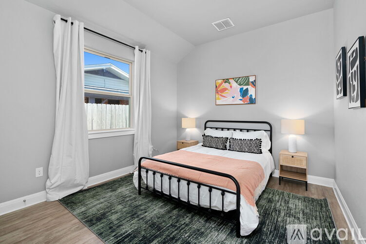 A bedroom with a large bed and a window with curtains.