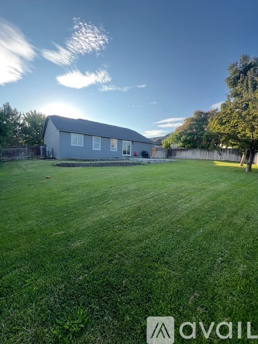 A house with a brown siding and a grey roof is surrounded by a fence and a grassy area.