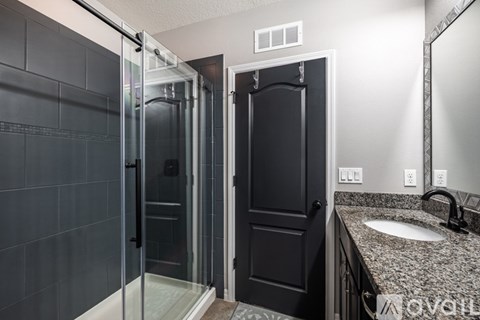 A bathroom with a black door and a glass shower stall.