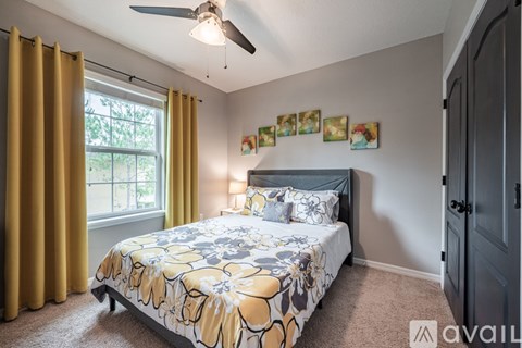 A bedroom with a bed, a ceiling fan, and a window with yellow curtains.