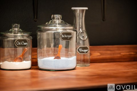Three glass containers with labels for Oxiclean, Detergent, and Vinger are on a wooden surface.