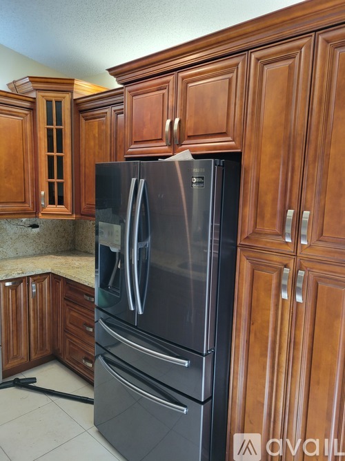 A black refrigerator with silver handles is in a kitchen with wooden cabinets.