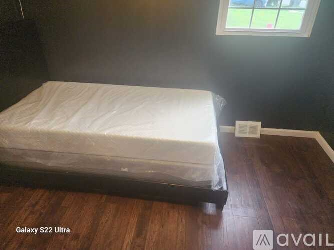 A white bed with a black frame is in a room with a wooden floor.