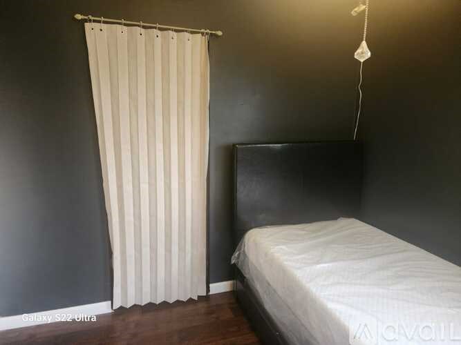 A bedroom with a bed, a hanging lamp, and a curtain.