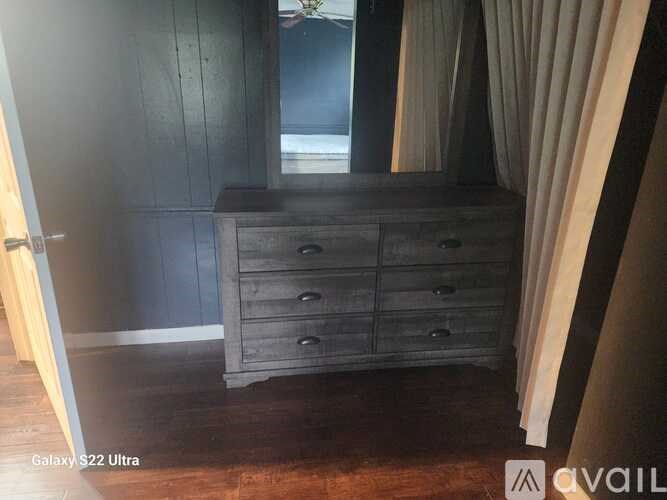 A wooden chest of drawers sits in a room with a curtain.
