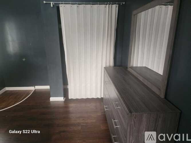 A room with a wooden floor and a bench with a window covered by white curtains.