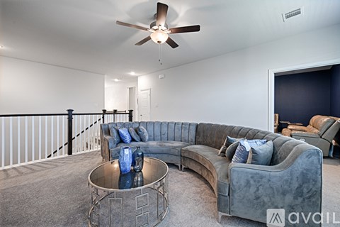 A living room with a grey couch and a round table with a blue vase on it.