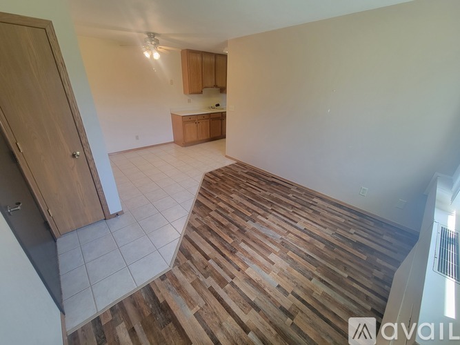 A room with wooden flooring and a kitchen area in the background.