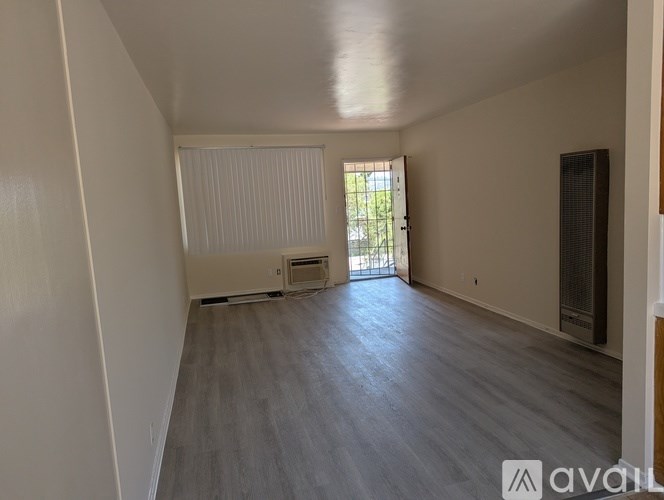 A spacious room with wooden flooring and a window with blinds.