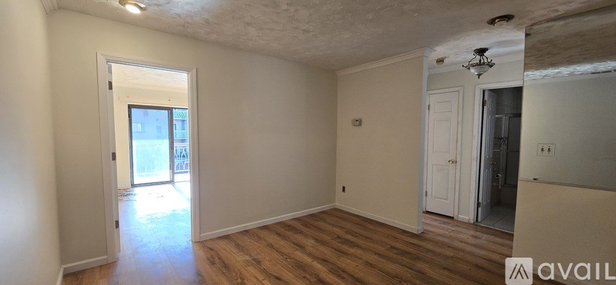 A room with wooden floors and white walls, with a door leading outside.