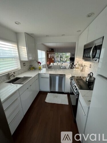 A modern kitchen with white cabinets and a wooden floor.
