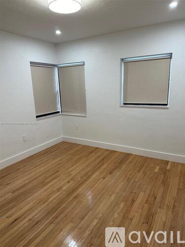 A room with wooden flooring and two windows.