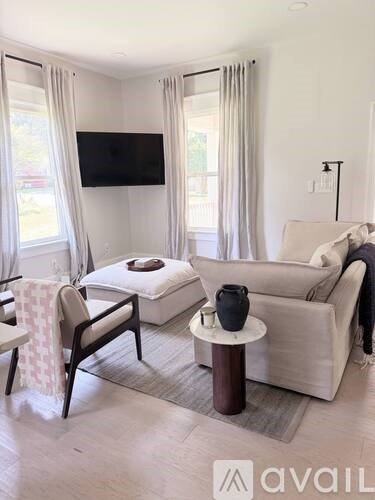 A living room with a white couch, a chair, a small table, and a television mounted on the wall.