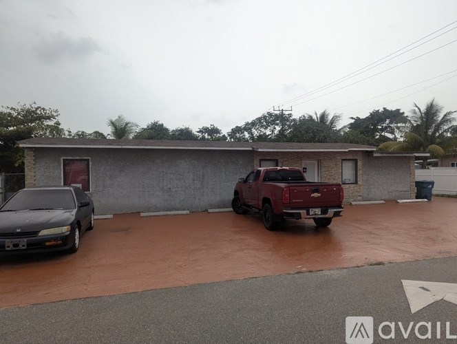 A black car is parked in front of a building with a red truck parked in front of it.