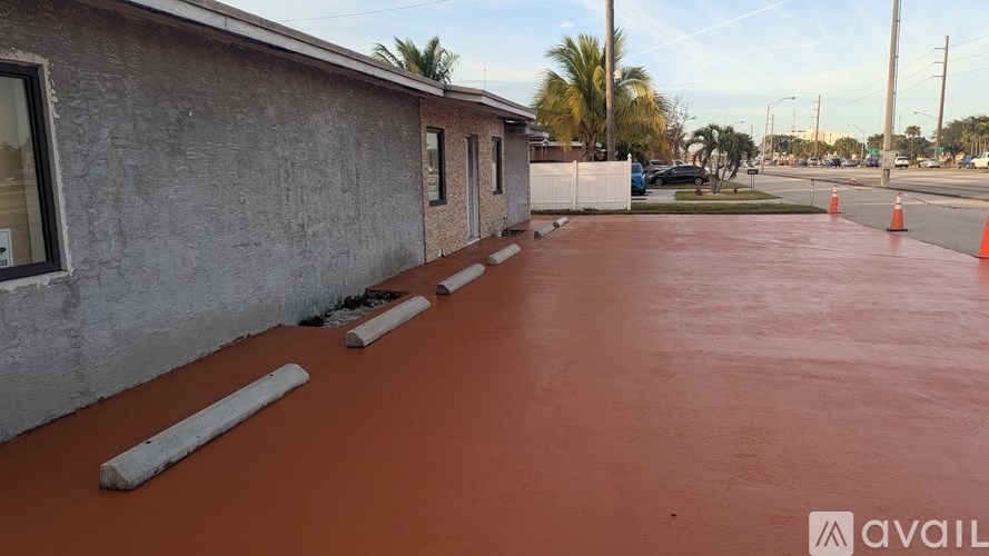 A parking lot with a building on the left and orange cones in the middle.