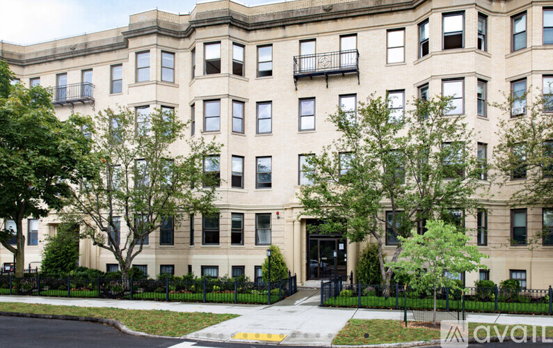 A large beige building with black railings and trees in front.