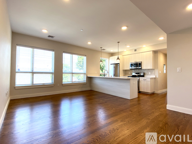 A spacious living room with hardwood floors and a kitchen area in the background.
