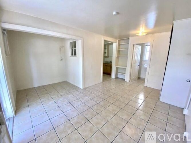 A spacious living room with white walls and tile flooring.