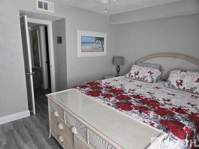 A bedroom with a bed, nightstand, and a painting of a beach scene on the wall.